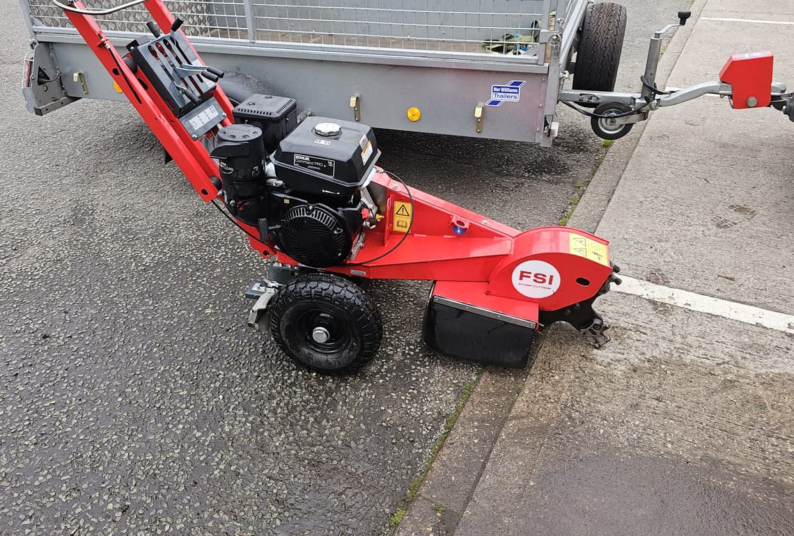 A red FSI pedestrian stump grinder on the yard beside the Ifor Williams caged trailer it travels on